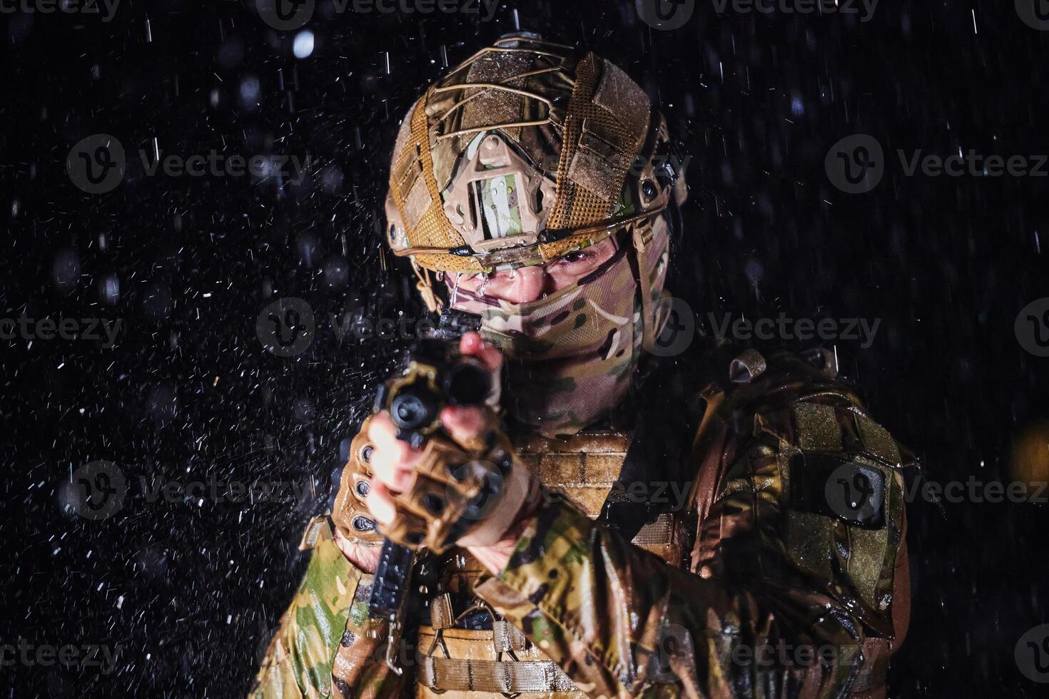 Army soldier in Combat Uniforms with an assault rifle, plate carrier and combat helmet going on a dangerous mission on a rainy night. photo