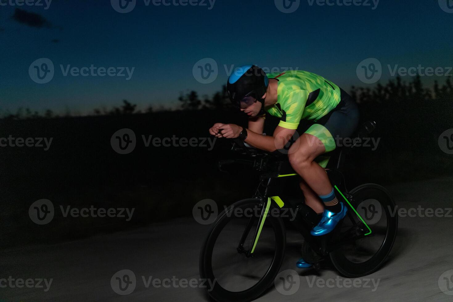 A triathlete rides his bike in the darkness of night, pushing himself to prepare for a marathon. The contrast between the darkness and the light of his bike creates a sense of drama and highlights the photo