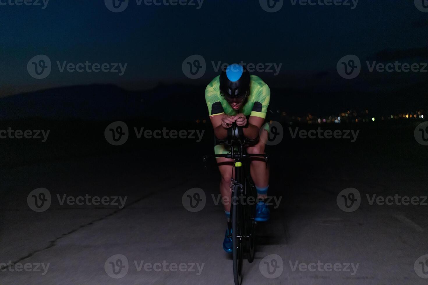 A triathlete rides his bike in the darkness of night, pushing himself to prepare for a marathon. The contrast between the darkness and the light of his bike creates a sense of drama and highlights the photo