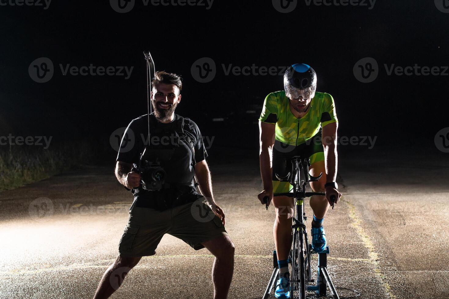 Behind the scenes. Professional videographer on a night shoot with a triathlete riding a bicycle for recording purposes photo