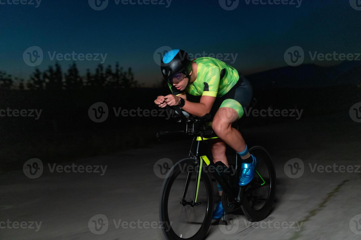 A triathlete rides his bike in the darkness of night, pushing himself to prepare for a marathon. The contrast between the darkness and the light of his bike creates a sense of drama and highlights the photo
