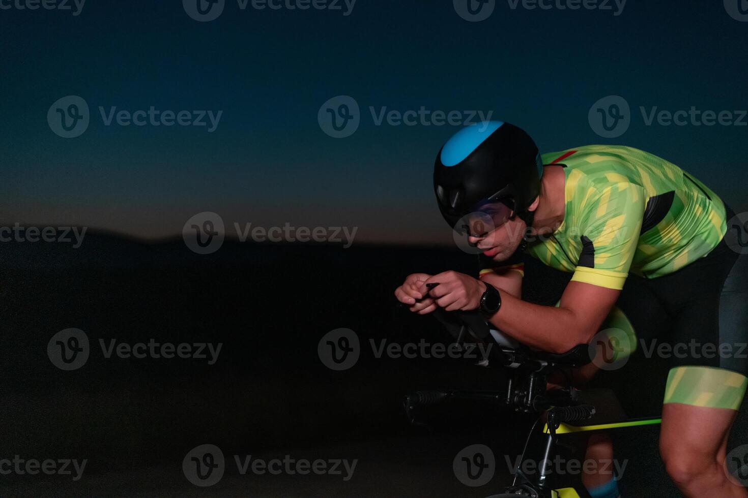 A triathlete rides his bike in the darkness of night, pushing himself to prepare for a marathon. The contrast between the darkness and the light of his bike creates a sense of drama and highlights the photo