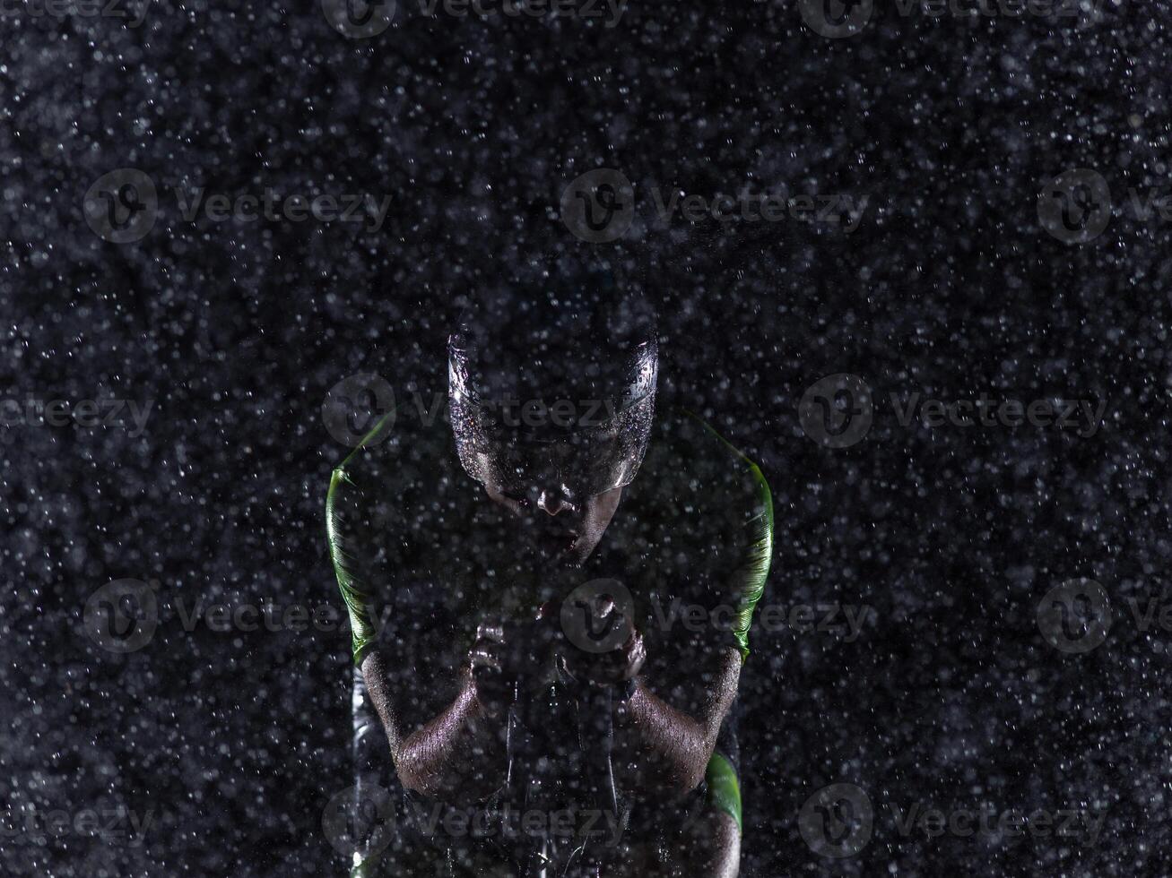 A triathlete braving the rain as he cycles through the night, preparing himself for the upcoming marathon. The blurred raindrops in the foreground and the dark, moody atmosphere in the background add photo