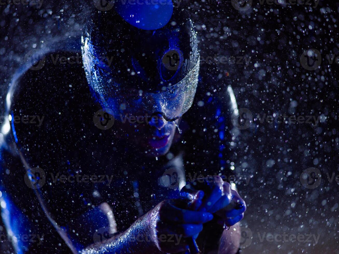 A triathlete braving the rain as he cycles through the night, preparing himself for the upcoming marathon. The blurred raindrops in the foreground and the dark, moody atmosphere in the background add photo