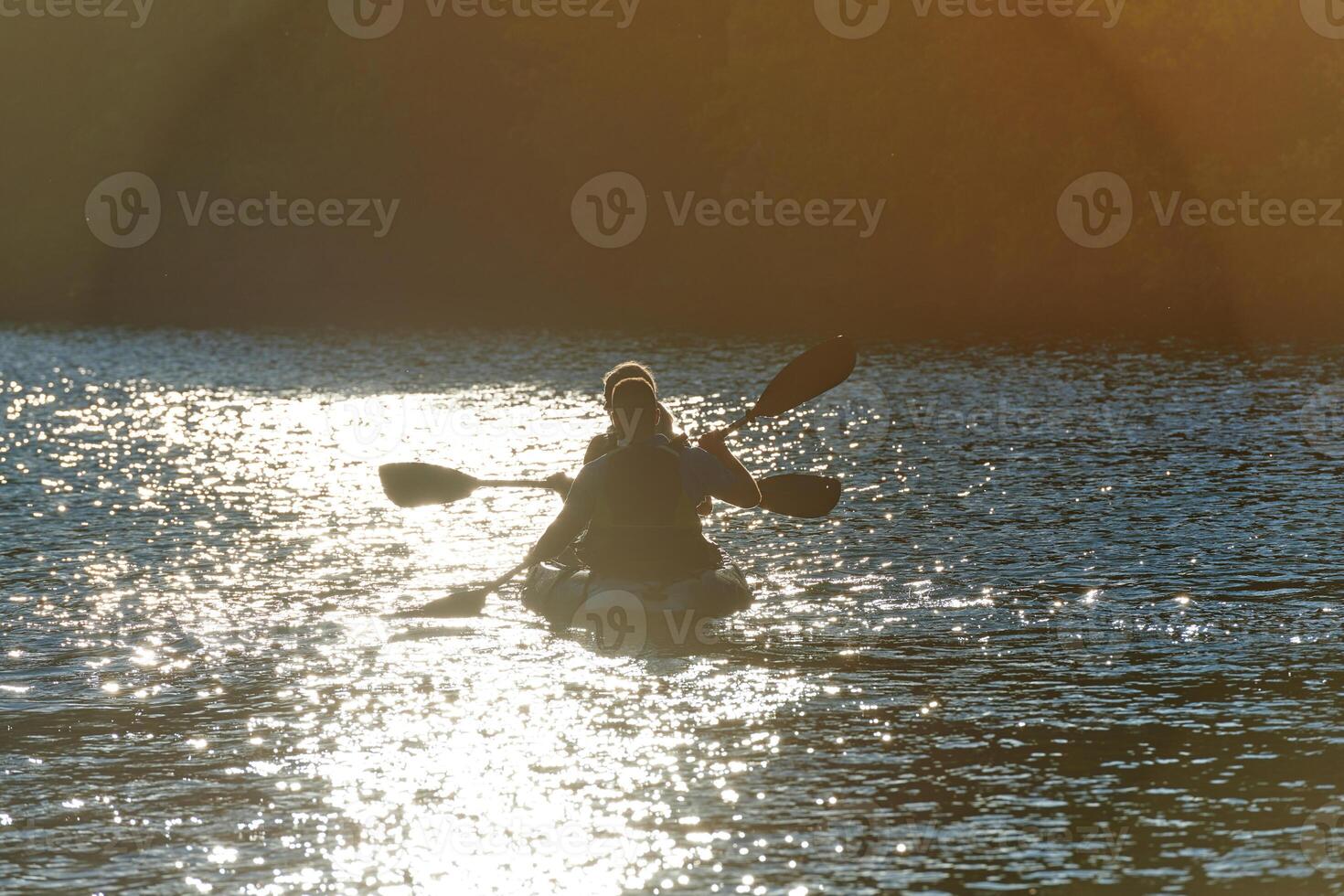 A young couple enjoying an idyllic kayak ride in the middle of a beautiful river surrounded by forest greenery in sunset time photo