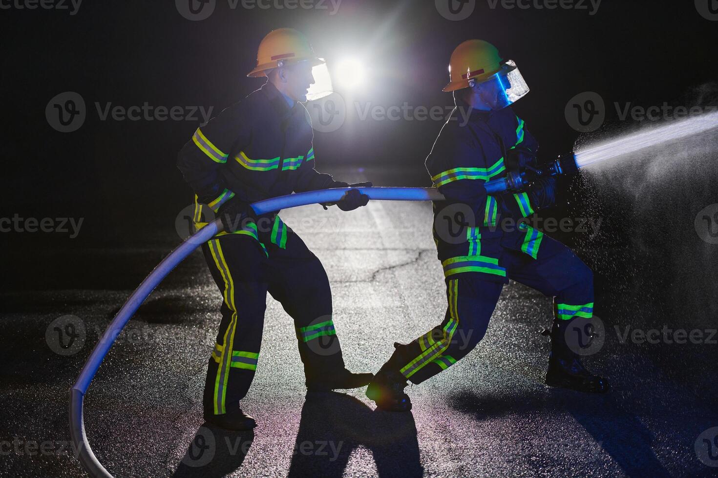 Firefighters using a water hose to eliminate a fire hazard. Team of female and male firemen in dangerous rescue mission. photo