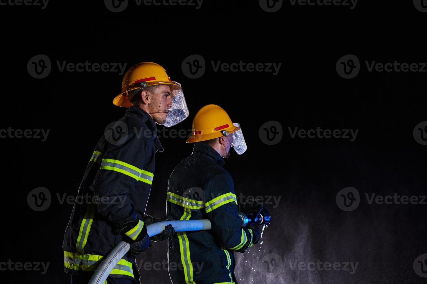 Firefighters using a water hose to eliminate a fire hazard. Team of female and male firemen in dangerous rescue mission. photo