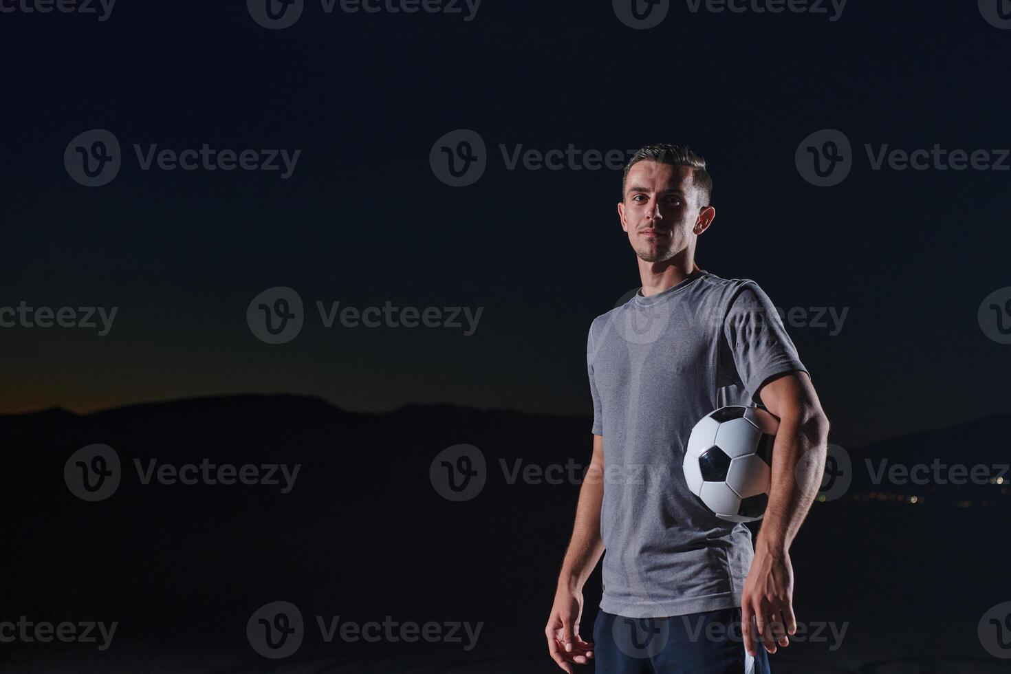 Portrait of a young handsome soccer player man on a street playing with a football ball. photo