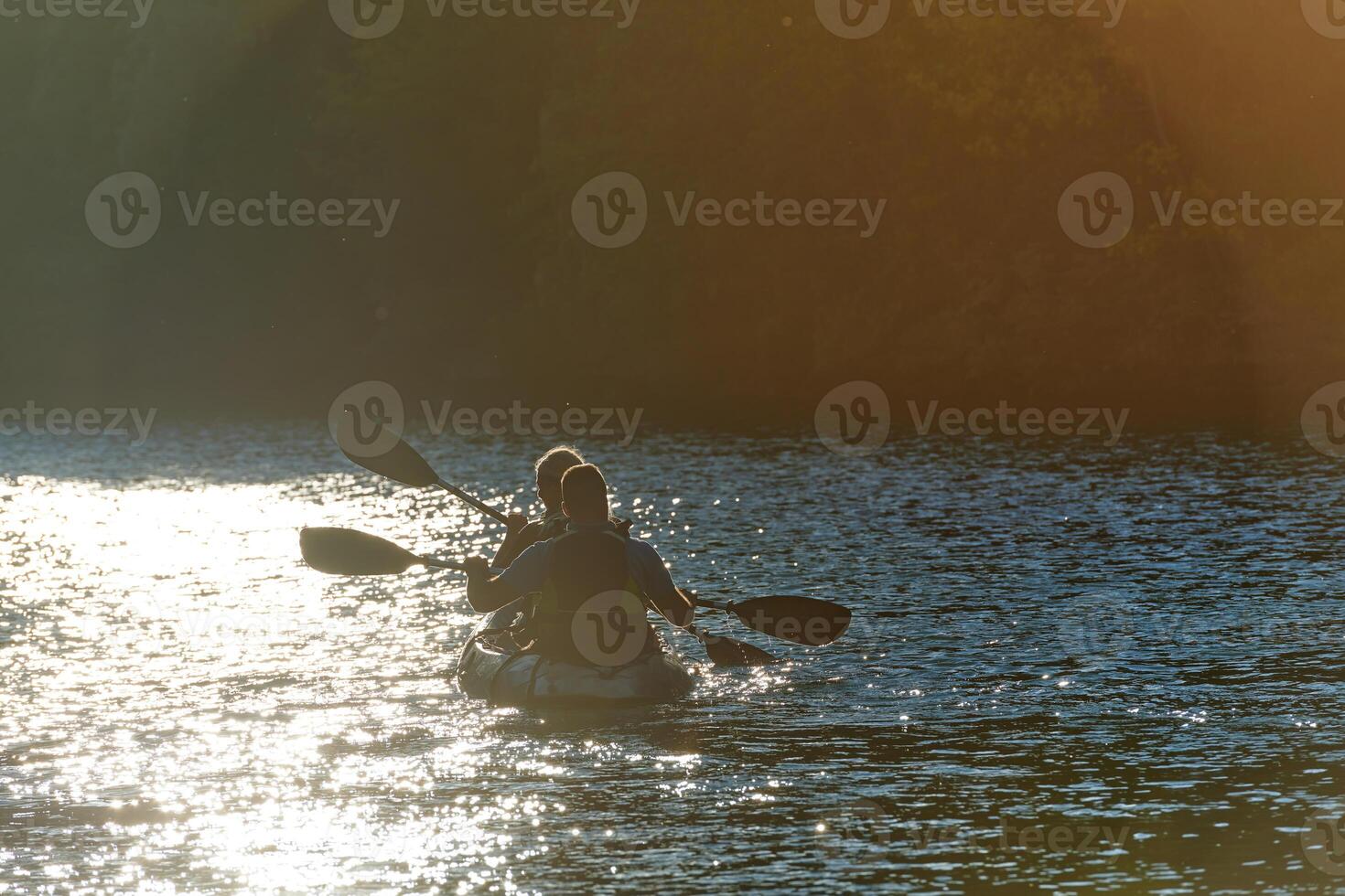 A young couple enjoying an idyllic kayak ride in the middle of a beautiful river surrounded by forest greenery in sunset time photo