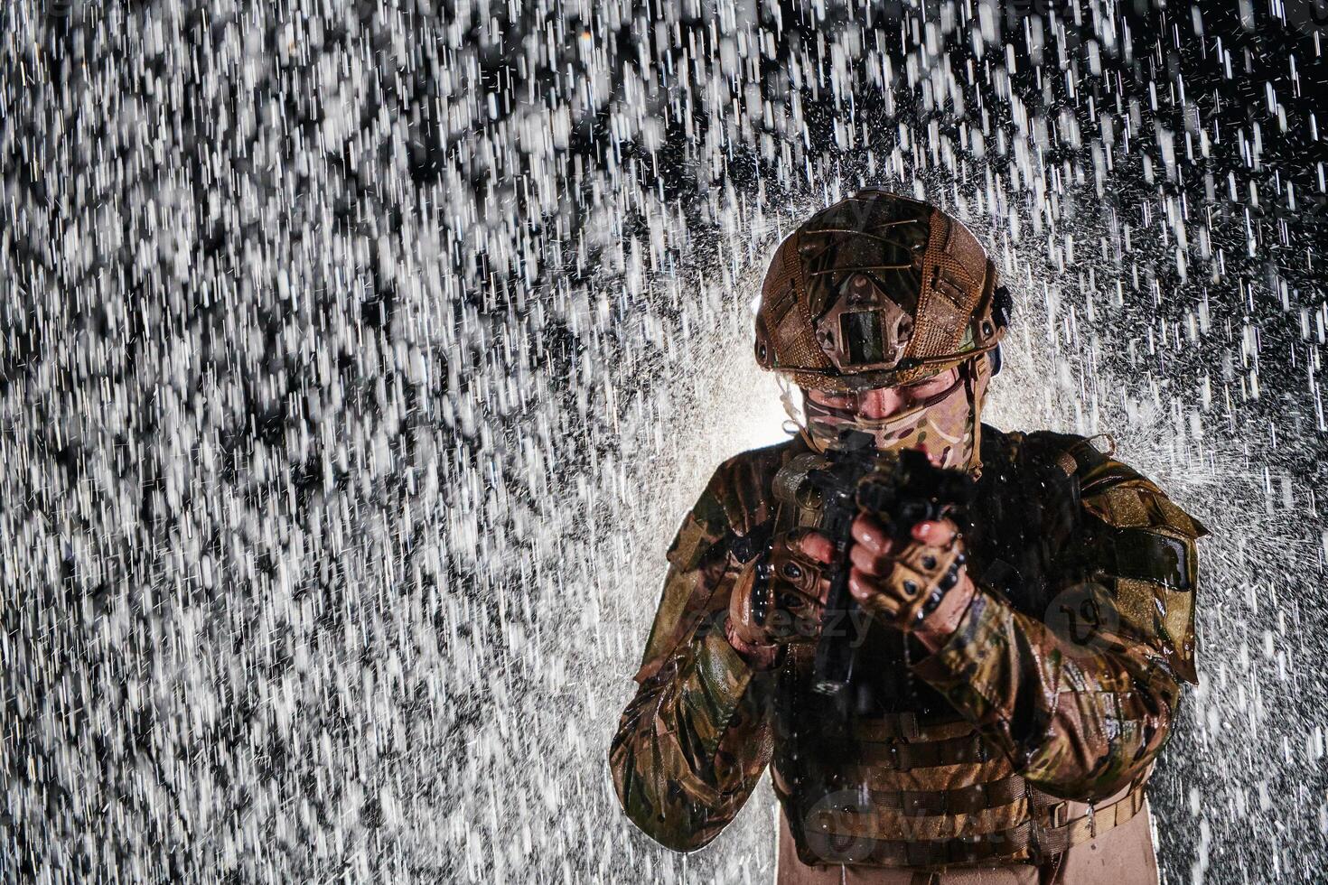 Army soldier in Combat Uniforms with an assault rifle, plate carrier and combat helmet going on a dangerous mission on a rainy night. photo