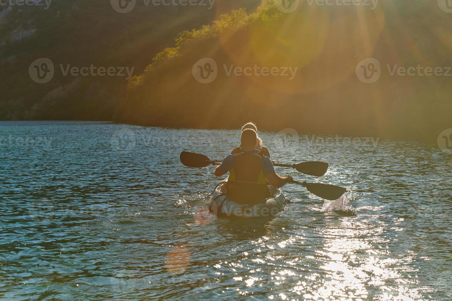A young couple enjoying an idyllic kayak ride in the middle of a beautiful river surrounded by forest greenery in sunset time photo