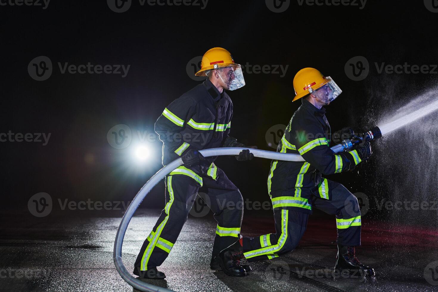 Firefighters using a water hose to eliminate a fire hazard. Team of female and male firemen in dangerous rescue mission. photo