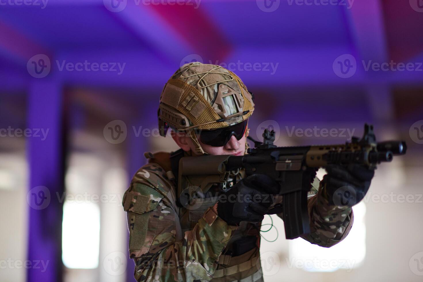 A professional soldier undertakes a perilous mission in an abandoned building illuminated by neon blue and purple lights photo