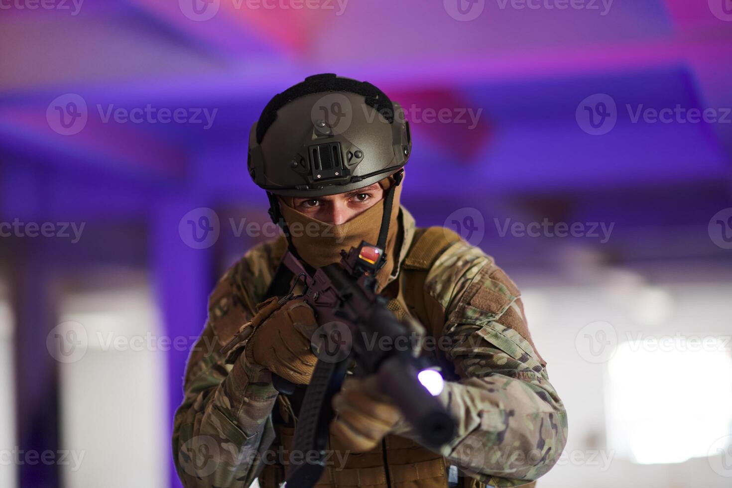 A professional soldier undertakes a perilous mission in an abandoned building illuminated by neon blue and purple lights photo