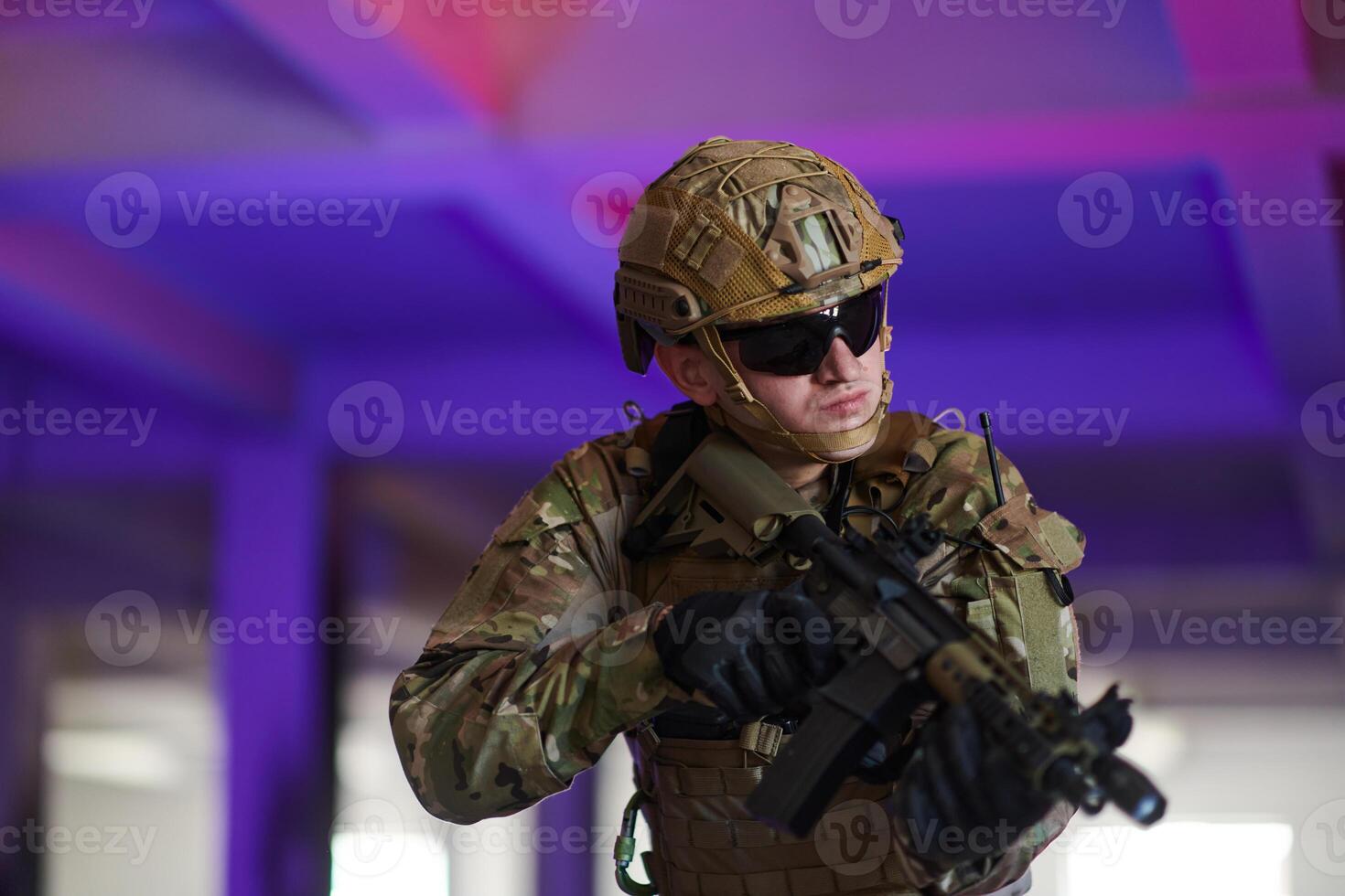 A professional soldier undertakes a perilous mission in an abandoned building illuminated by neon blue and purple lights photo