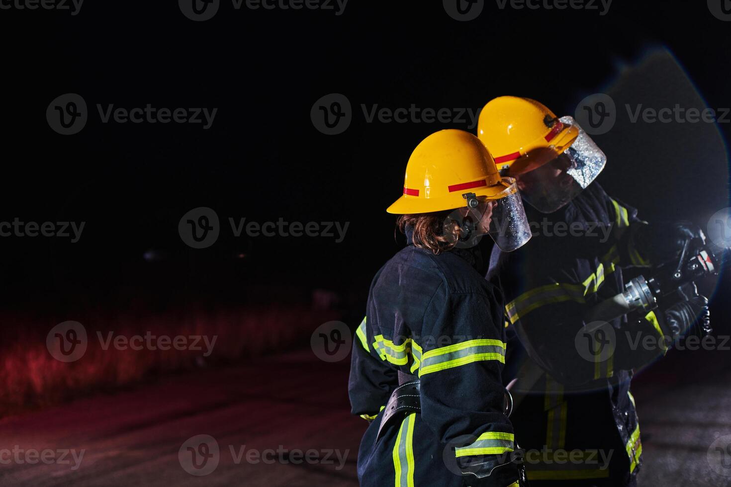 Firefighters using a water hose to eliminate a fire hazard. Team of female and male firemen in dangerous rescue mission. photo