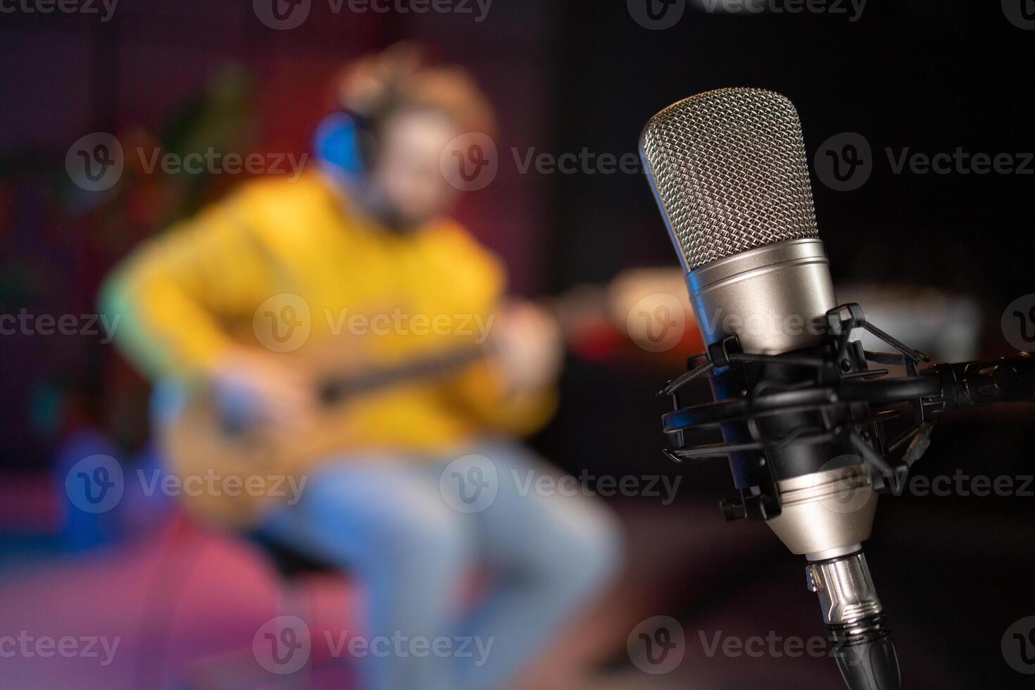 A focused male musician fine-tunes a bass guitar against the backdrop of a digital sound editing setup in a contemporary recording studio environment. Copy space photo