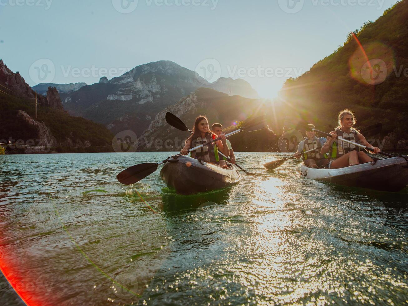 A group of friends enjoying fun and kayaking exploring the calm river, surrounding forest and large natural river canyons during an idyllic sunset. photo