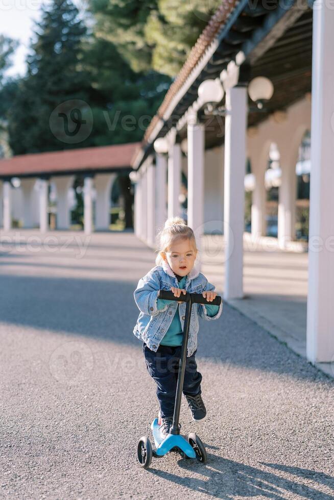 Little girl with her mouth open rides a scooter along the road in the park photo