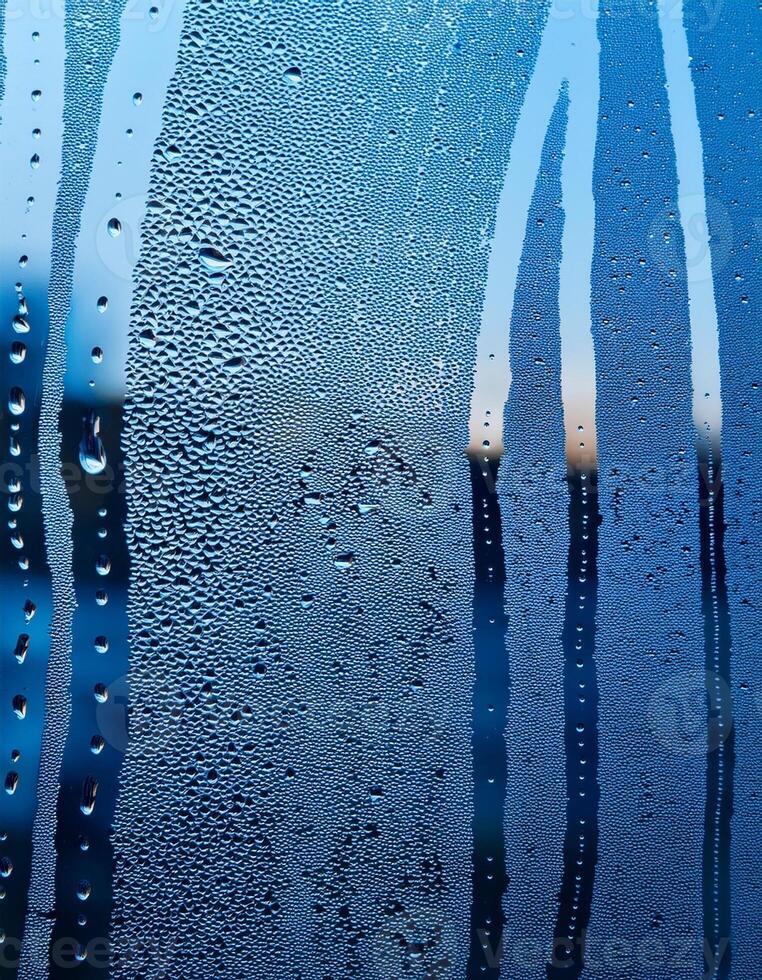Condensation Forms Water Droplets on a Glass Window With Blue and Orange Hues in the Background During Early Morning Hours photo