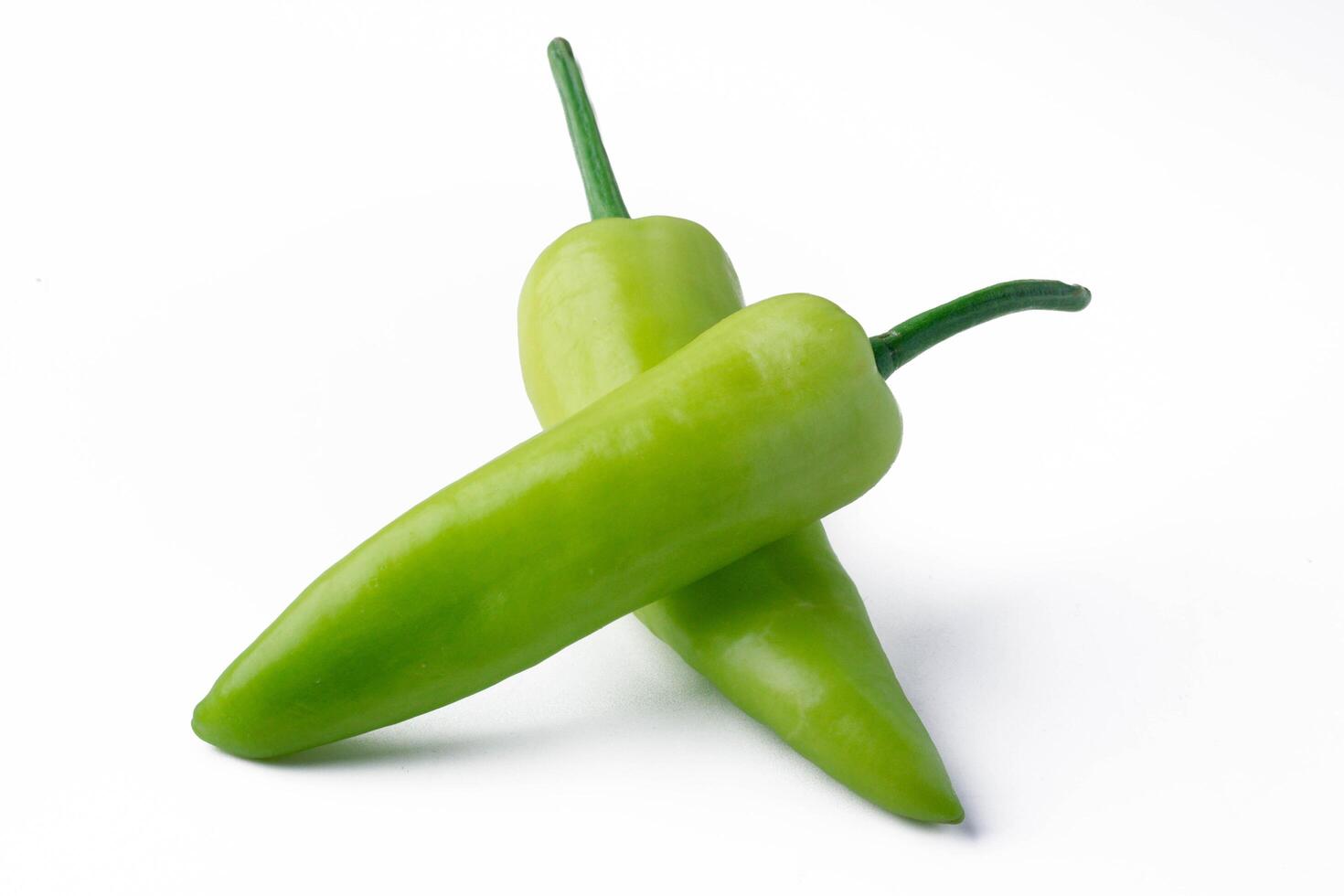 Two fresh green chili peppers are placed on white background, showcasing their vibrant color and smooth texture photo