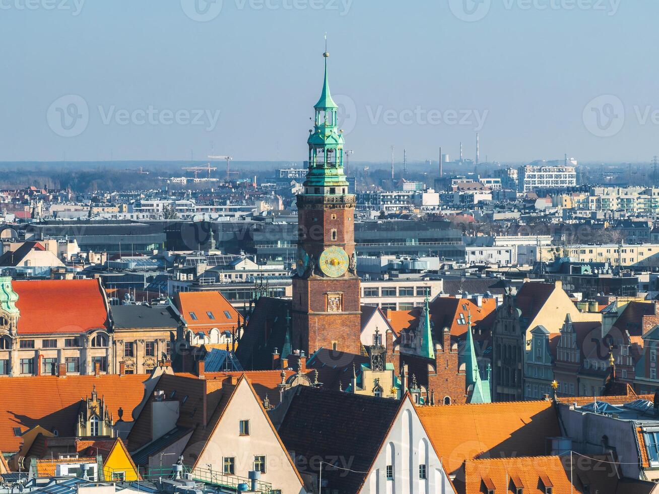 Aerial view of Wroclaw, Poland, featuring the Gothic style Old Town Hall tower with a green spire, surrounded by historic red tiled buildings and modern structures. photo
