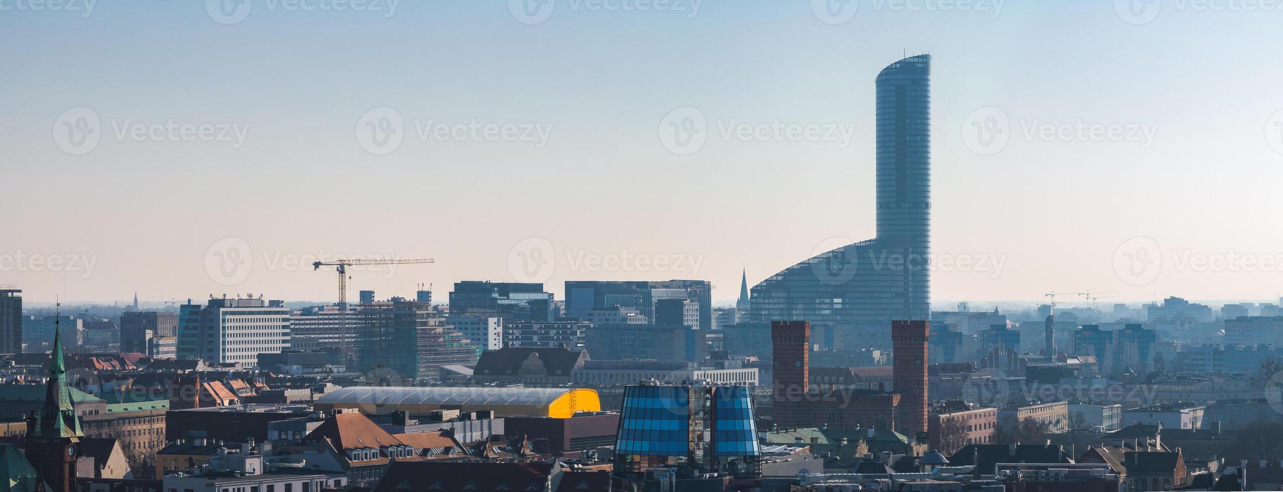 Aerial view of Wroclaw, Poland, showcasing the Sky Tower, red brick buildings, modern glass facades, and construction cranes under a clear sky. photo