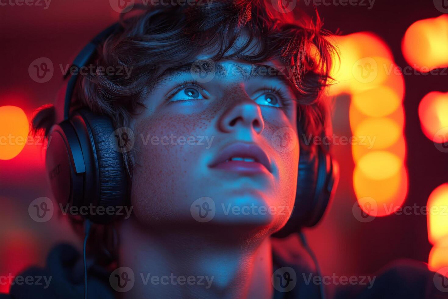 a teenage boy livestreaming on a gaming platform, wearing headphones and interacting with his audience, with a vibrant LED-lit setup and focused expression photo