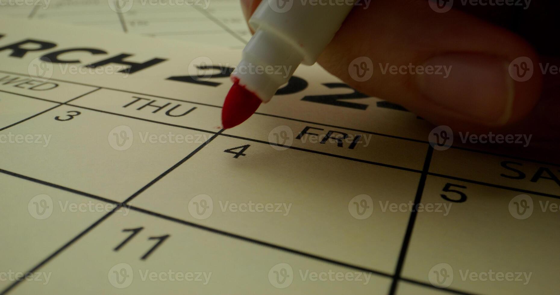 A person is writing on a calendar with a red pen photo