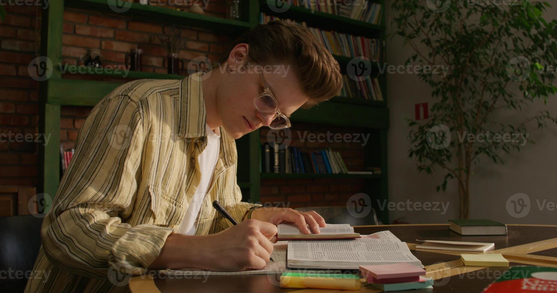 A young man is sitting at a table with a book and pen photo