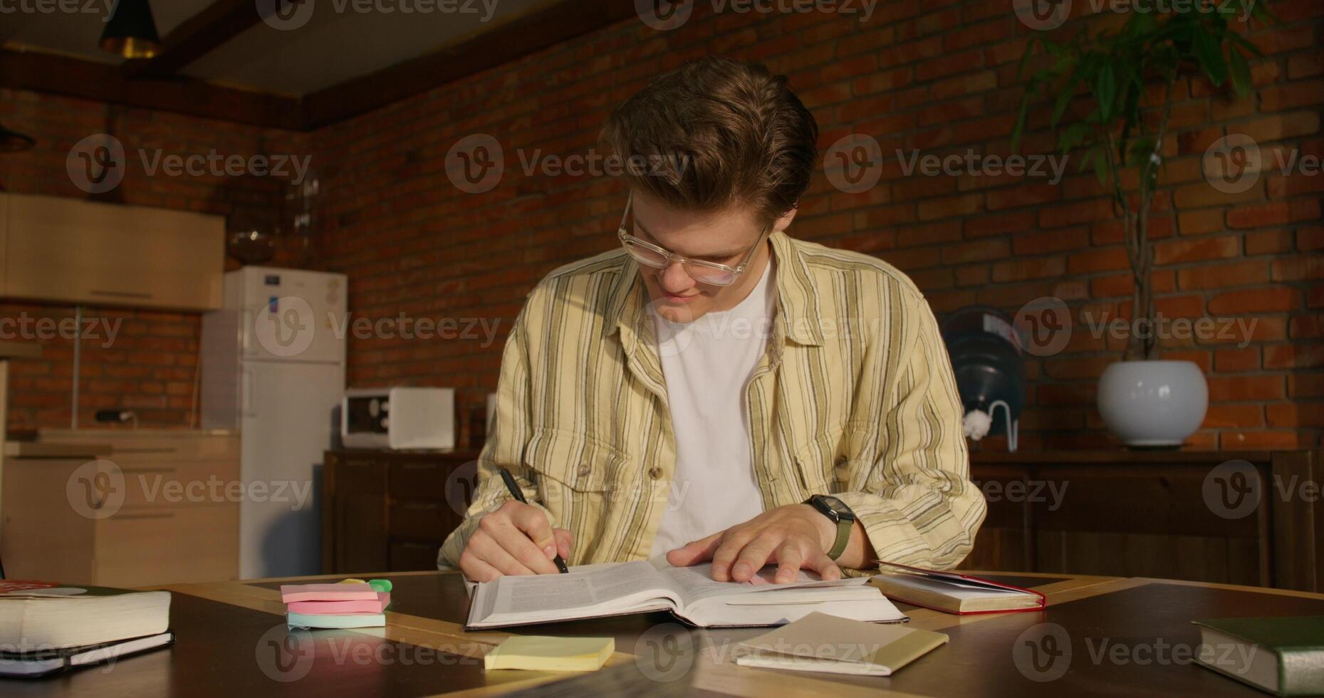 A man in glasses is writing in a book photo