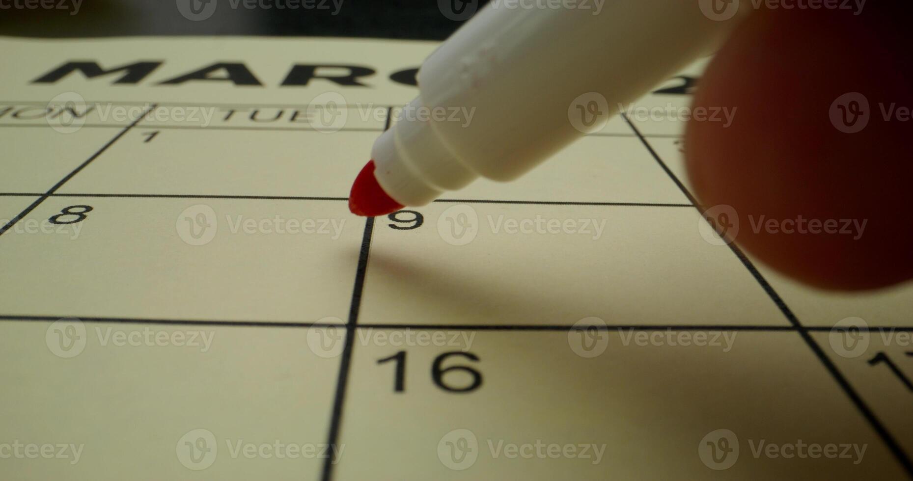 A person is writing on a calendar with a red marker photo