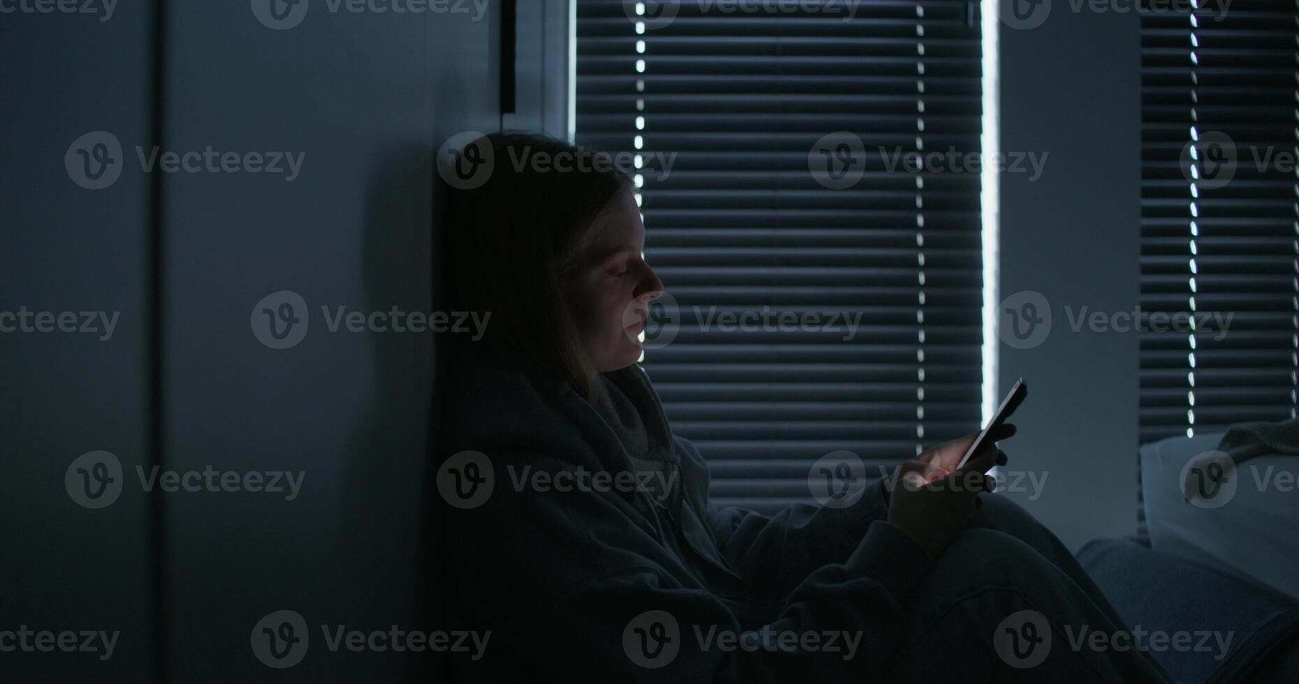 A woman sitting in a dark room with a cell phone photo