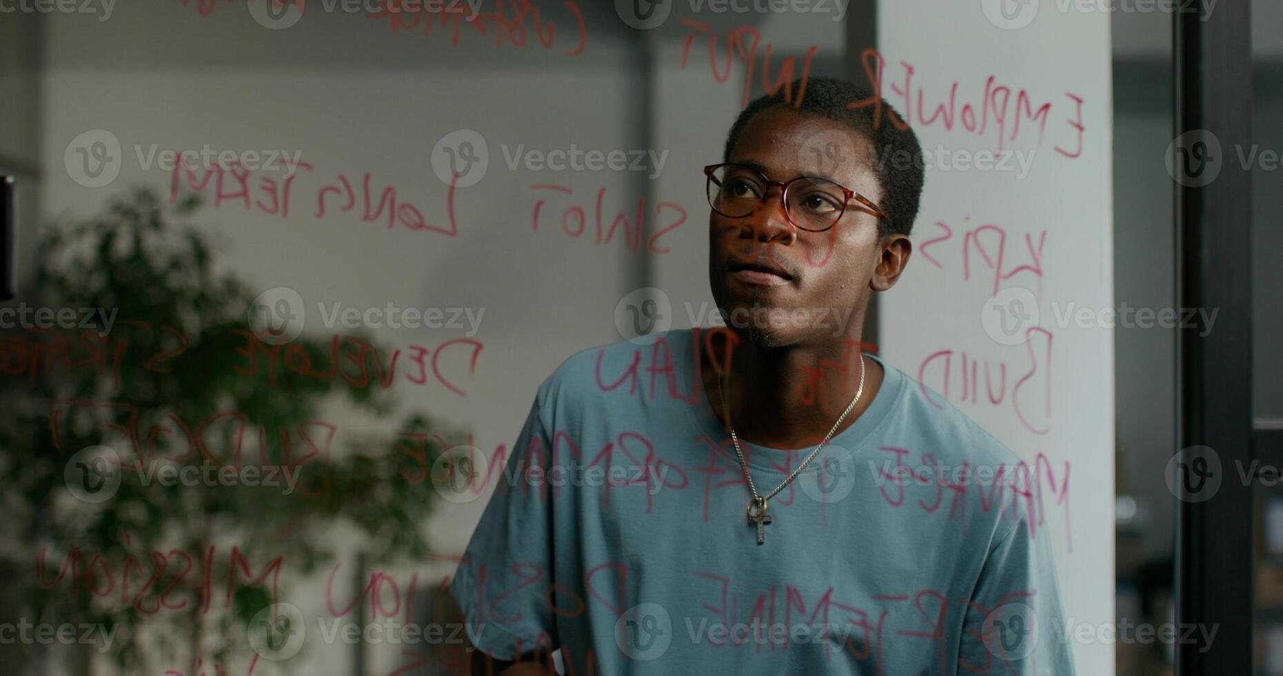 A man with glasses and a blue shirt is looking at a wall with writing on it photo
