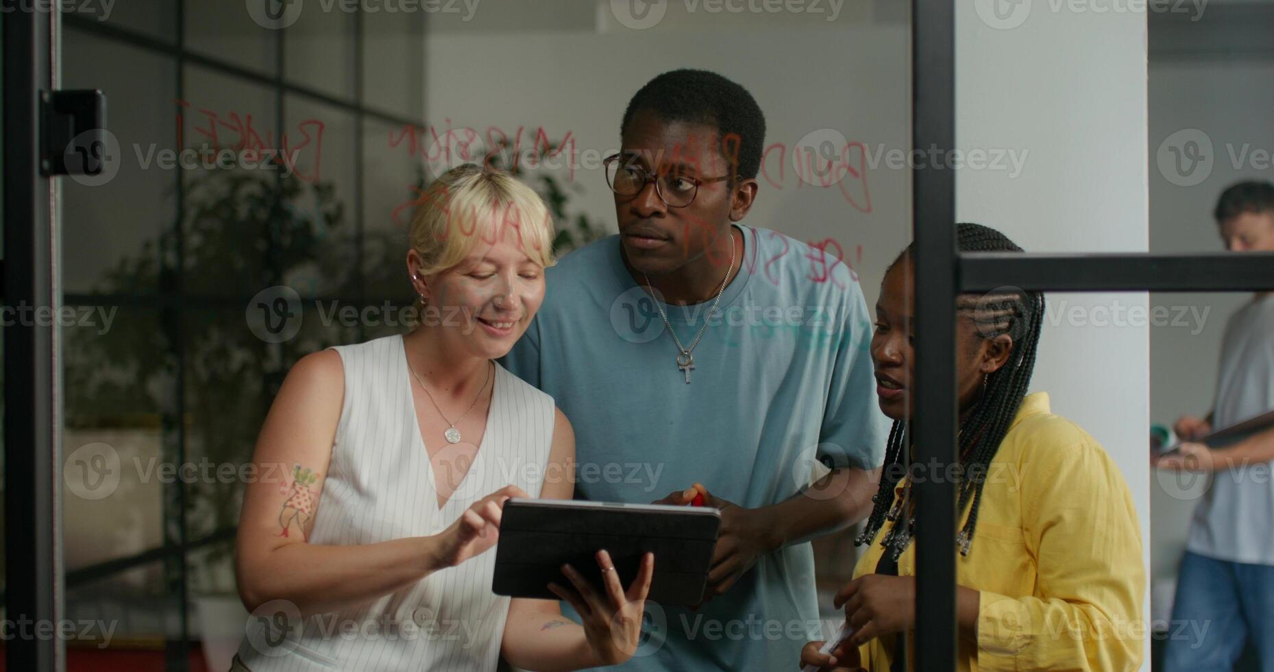 Three people standing in front of a glass door looking at a tablet photo