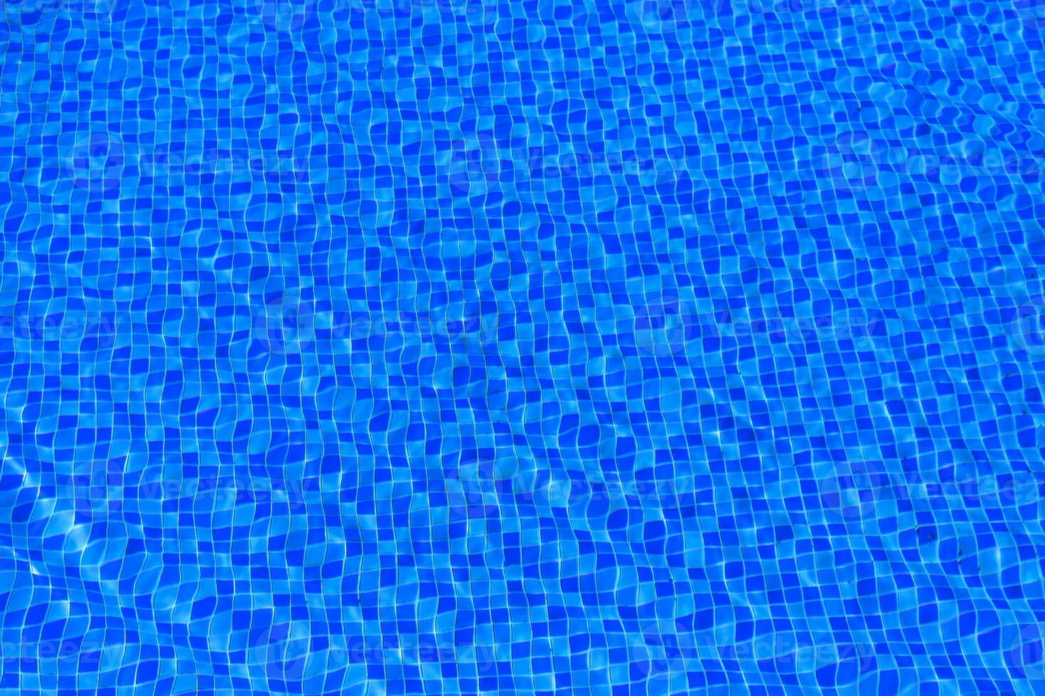 Water ripples on blue tiled swimming pool background. Blue turquoise pool water. Ripples lit up by the sun. Tiles visible below. Top view. photo