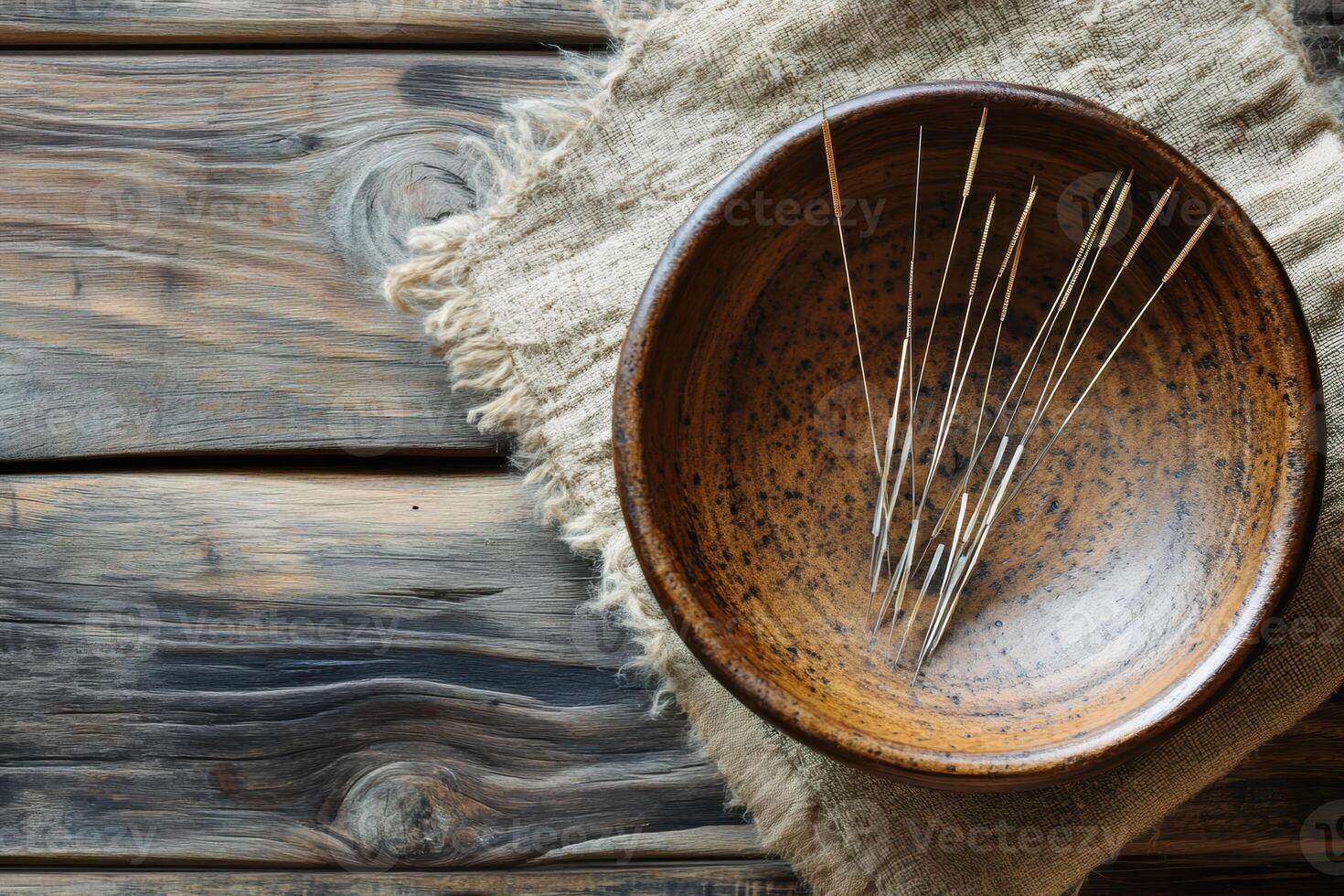Rustic wooden table with brown ceramic bowl and acupuncture needles on burlap fabric. Top view photo