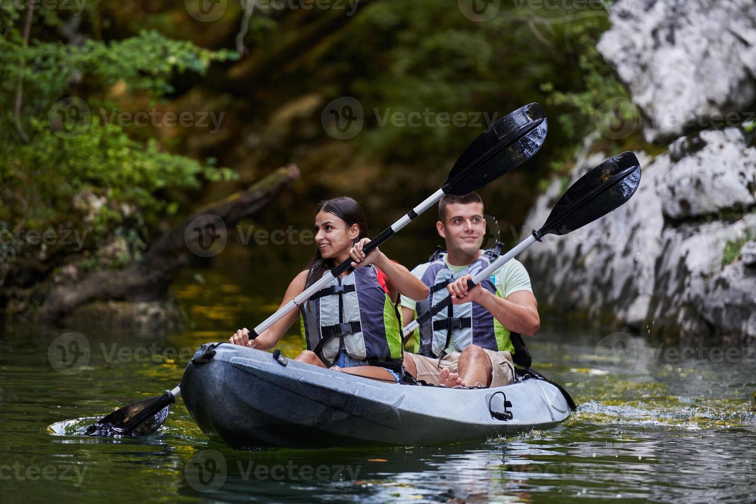 A young couple enjoying an idyllic kayak ride in the middle of a beautiful river surrounded by forest greenery photo