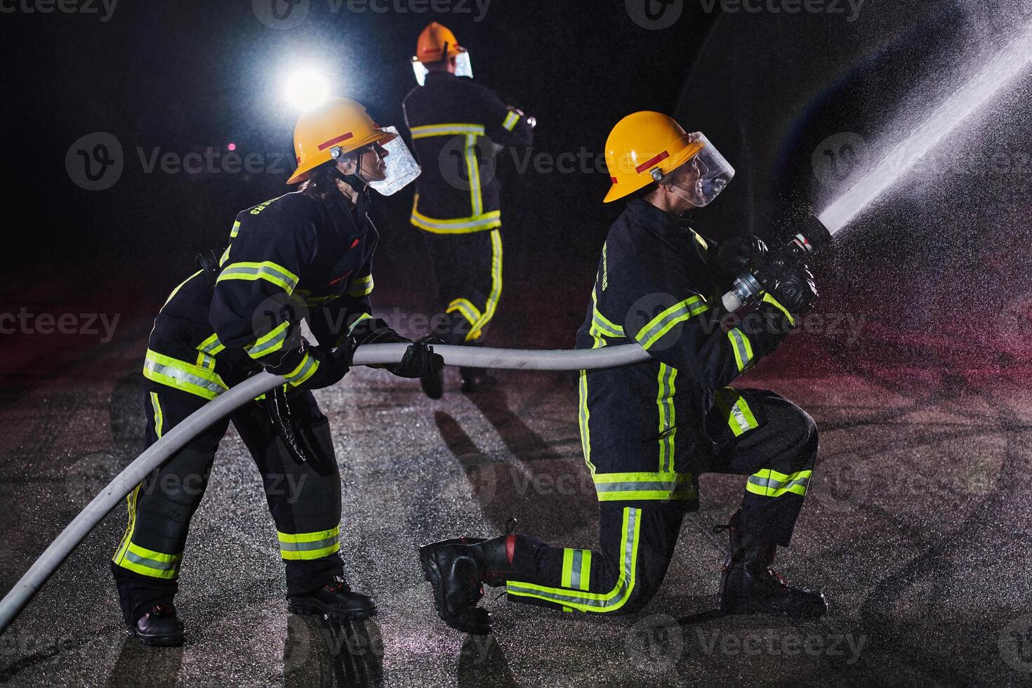 Firefighters using a water hose to eliminate a fire hazard. Team of female and male firemen in dangerous rescue mission. photo