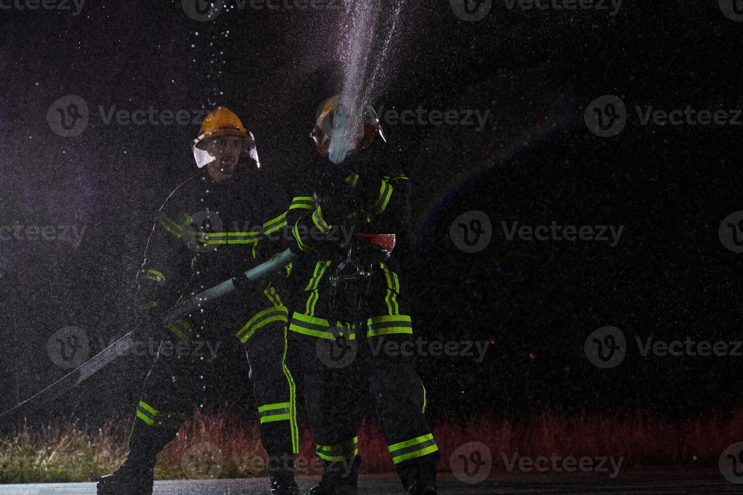 Firefighters using a water hose to eliminate a fire hazard. Team of female and male firemen in dangerous rescue mission. photo