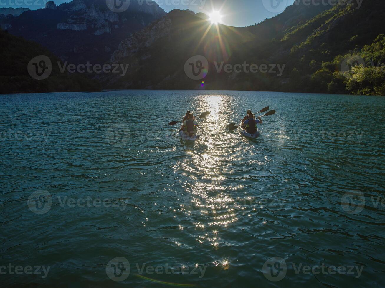 A group of friends enjoying fun and kayaking exploring the calm river, surrounding forest and large natural river canyons during an idyllic sunset. photo