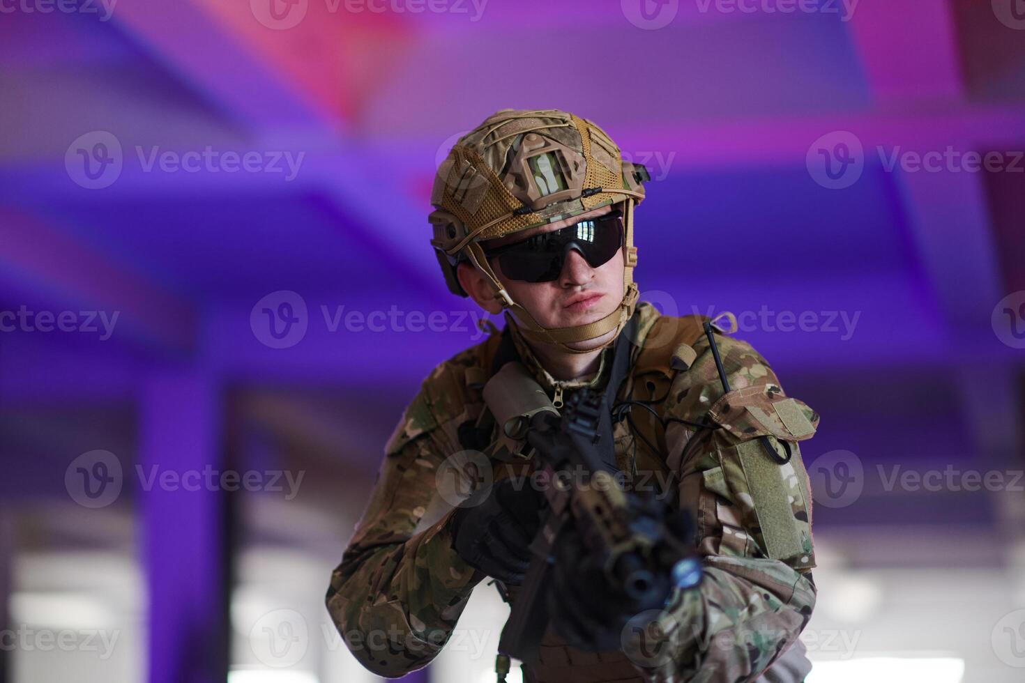 A professional soldier undertakes a perilous mission in an abandoned building illuminated by neon blue and purple lights photo