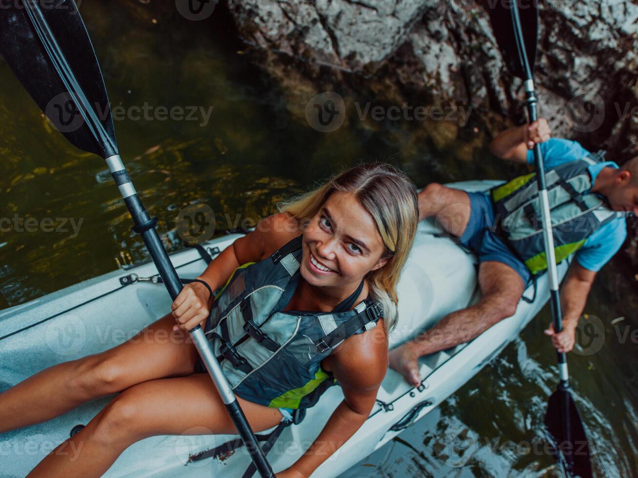 A young couple enjoying an idyllic kayak ride in the middle of a beautiful river surrounded by forest greenery photo