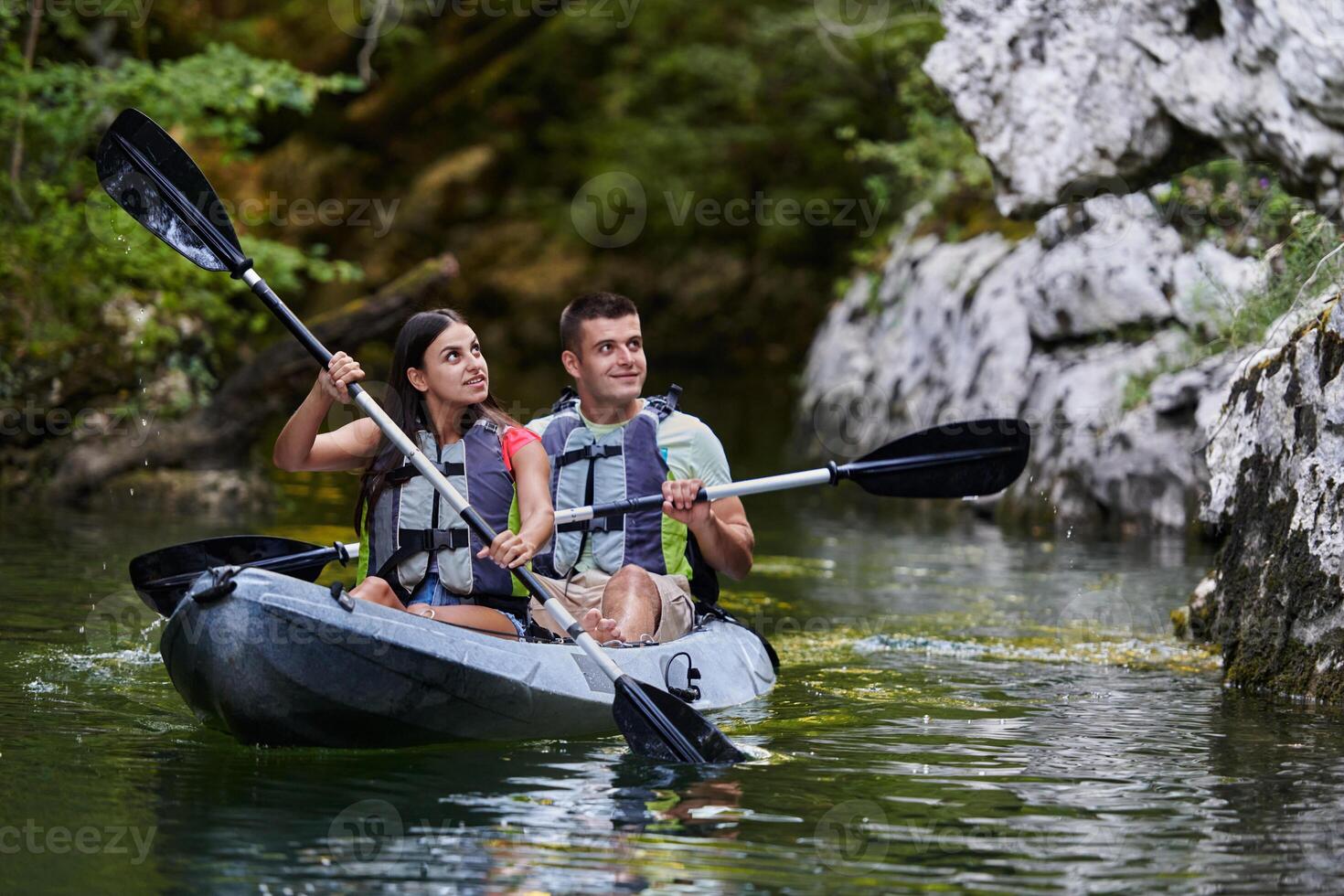 A young couple enjoying an idyllic kayak ride in the middle of a beautiful river surrounded by forest greenery photo