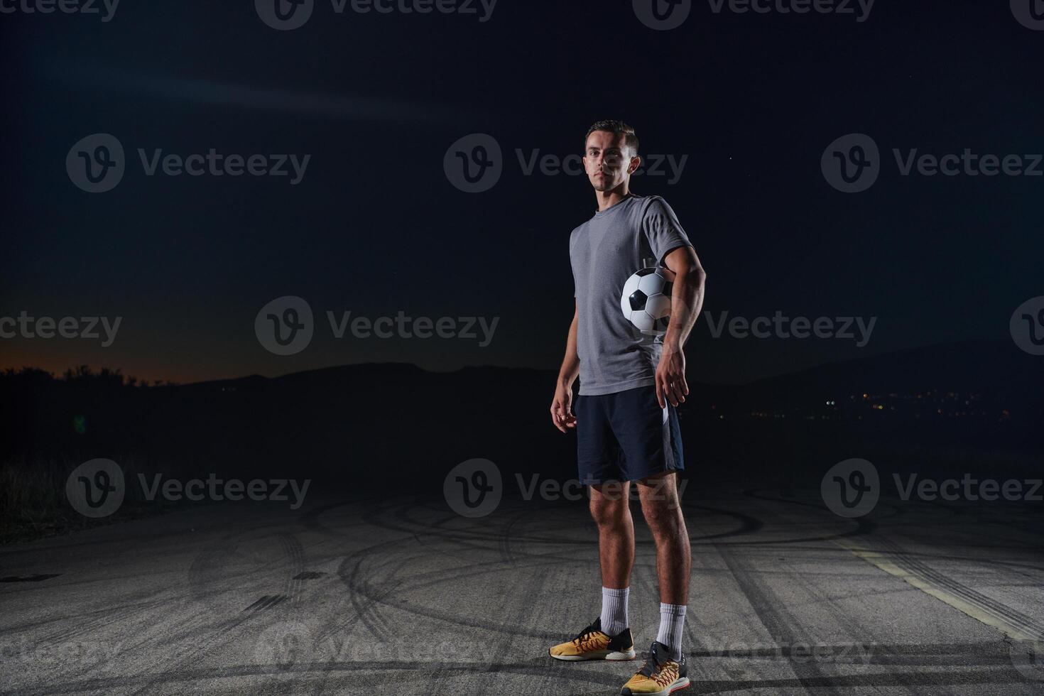 Portrait of a young handsome soccer player man on a street playing with a football ball. photo