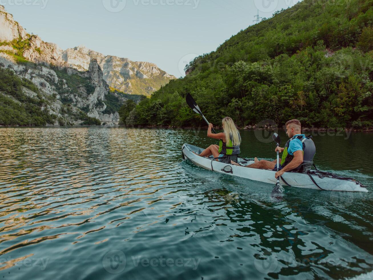 A young couple enjoying an idyllic kayak ride in the middle of a beautiful river surrounded by forest greenery photo