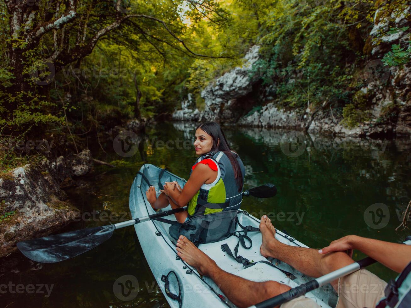 A young couple enjoying an idyllic kayak ride in the middle of a beautiful river surrounded by forest greenery photo