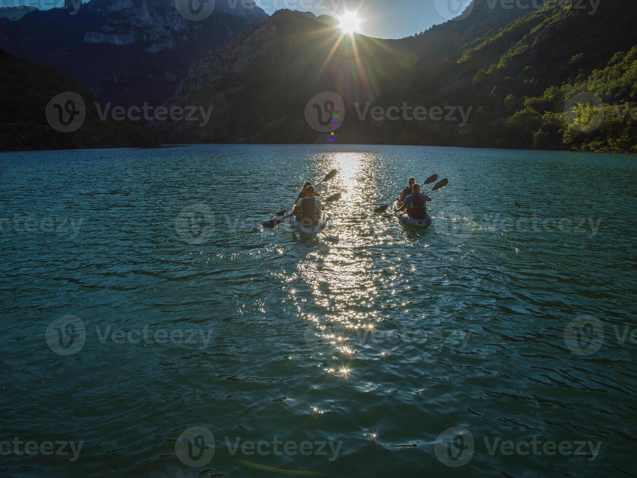 A group of friends enjoying fun and kayaking exploring the calm river, surrounding forest and large natural river canyons during an idyllic sunset. photo