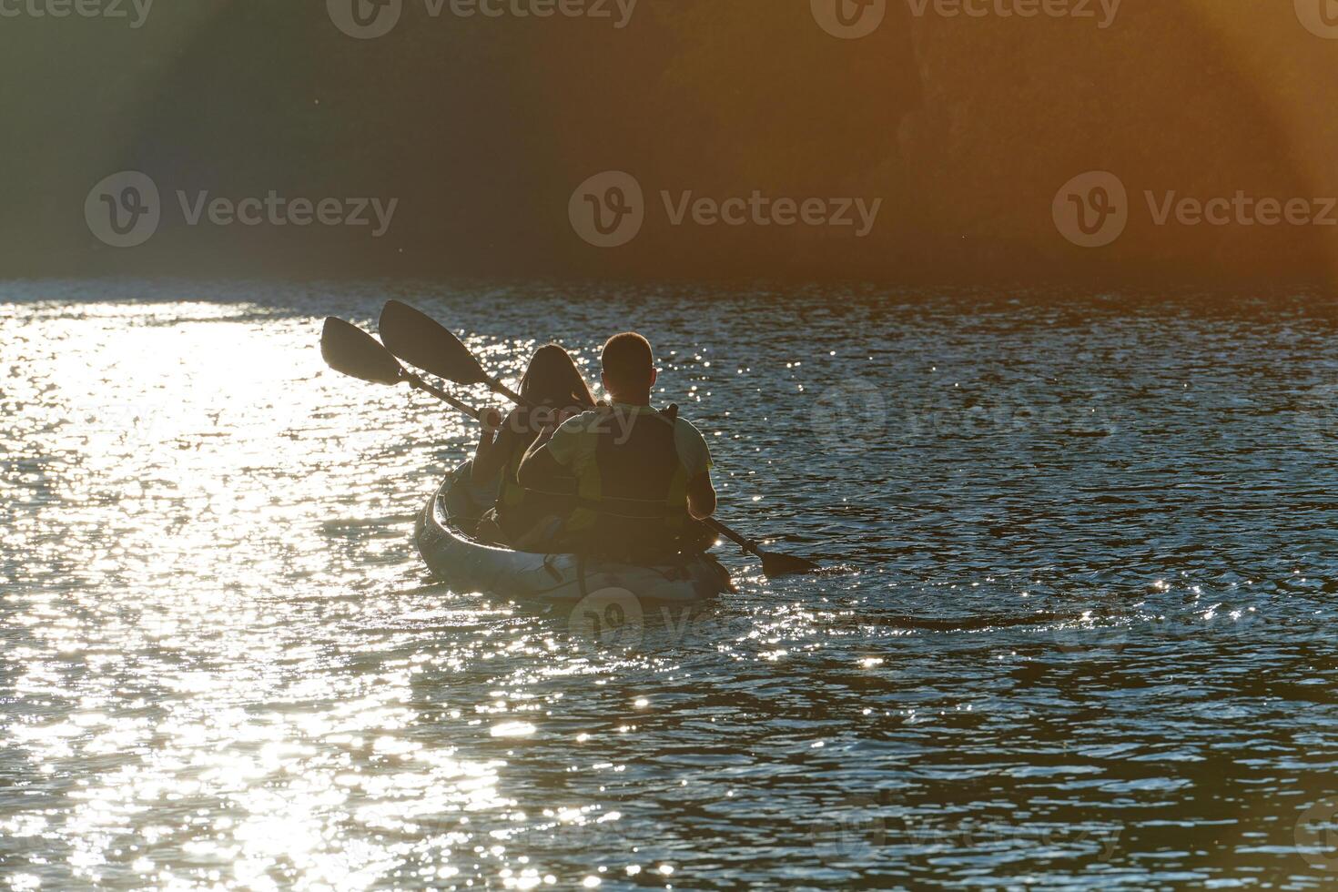 A young couple enjoying an idyllic kayak ride in the middle of a beautiful river surrounded by forest greenery in sunset time photo