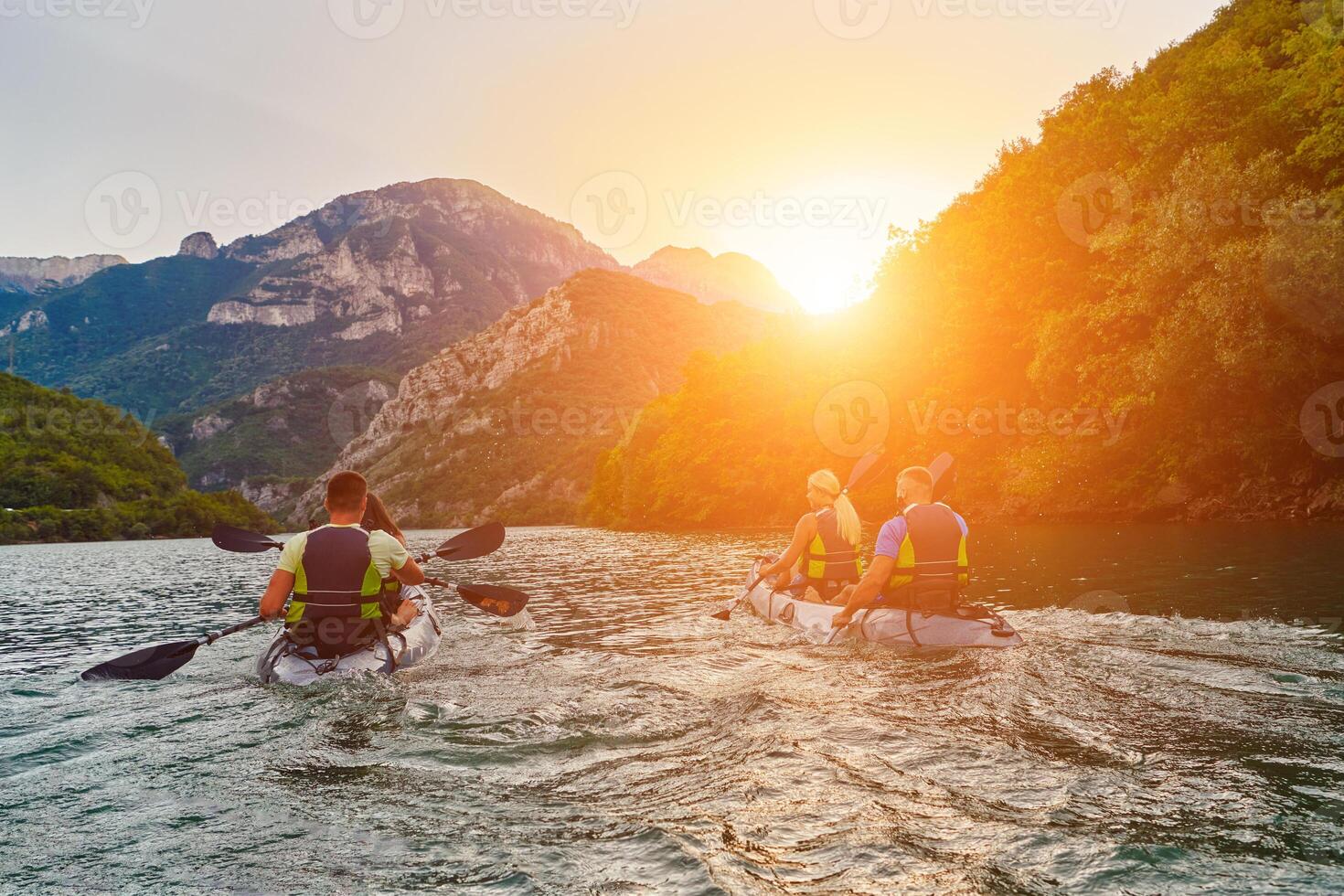 A group of friends enjoying fun and kayaking exploring the calm river, surrounding forest and large natural river canyons during an idyllic sunset. photo
